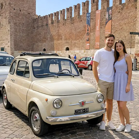 Una coppia in piedi accanto alla Fiat 500 crema nel piazzale di Castelvecchio, sotto le merlature di mattoni