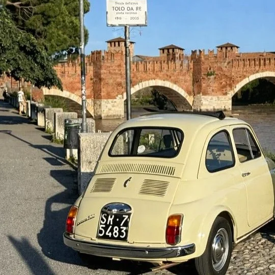 Il ponte di Castelvecchio con le merlature e le arcate di mattoni, e la Fiat 500 crema ferma sull'argine dell'Adige
